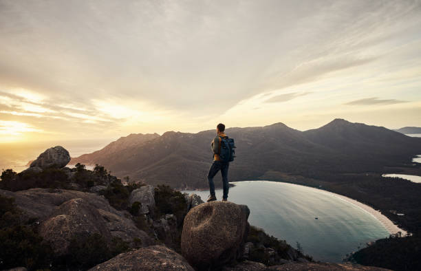 He loves the great outdoors Rearview shot of a young man taking in the view while standing on a mountain peak explorer stock pictures, royalty-free photos & images