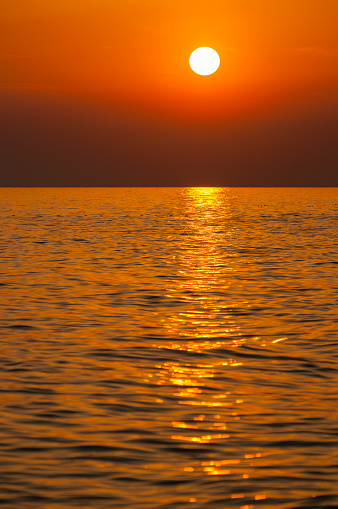 Bright orange sunset over Adriatic sea with radiant setting sun reflecting on water