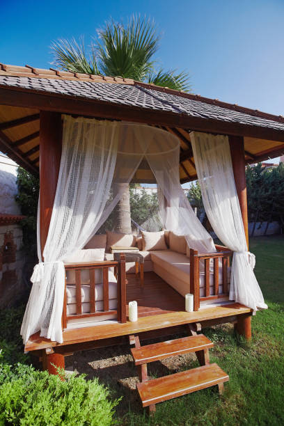 istock Wooden gazebo on green grass with soft sofa and pillows for relaxing 938565820