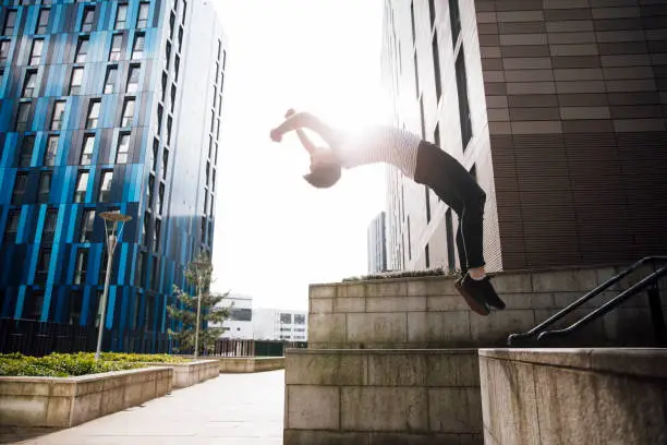 Freerunner is doing a backflip off a wall in the city.