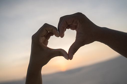 Close-up on coupleâs hands making a heart shape â relationship concepts