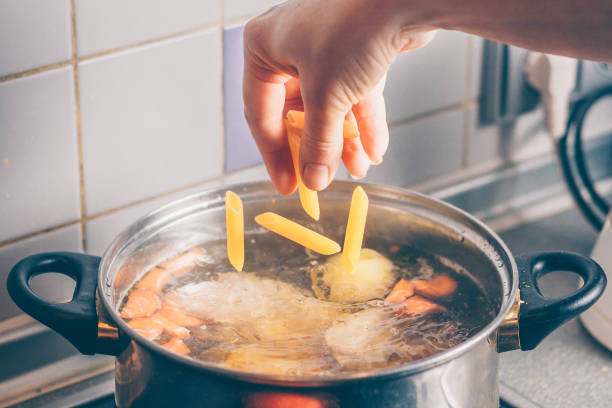 The cook adds macaroni to the soup