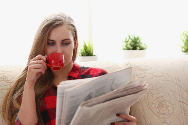 kobieta pije kawę i czytanie siedzieć na kanapie - reading newspaper break tea zdjęcia i obrazy z banku zdjęć