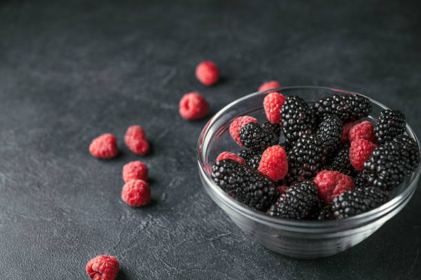 istock Glass plate with ripe red blackberries and raspberries on a black surface. 938581832