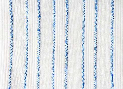 Vertical white stripes of knitted fabric and thick embossed fabric are connected by a blue zigzag stitch.
