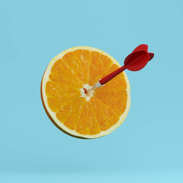 istock Orange fruit with circular target marked and red dart on pastel blue background. minimal idea food and fruit concept. An idea creative to produce work within an advertising marketing communications 938613436