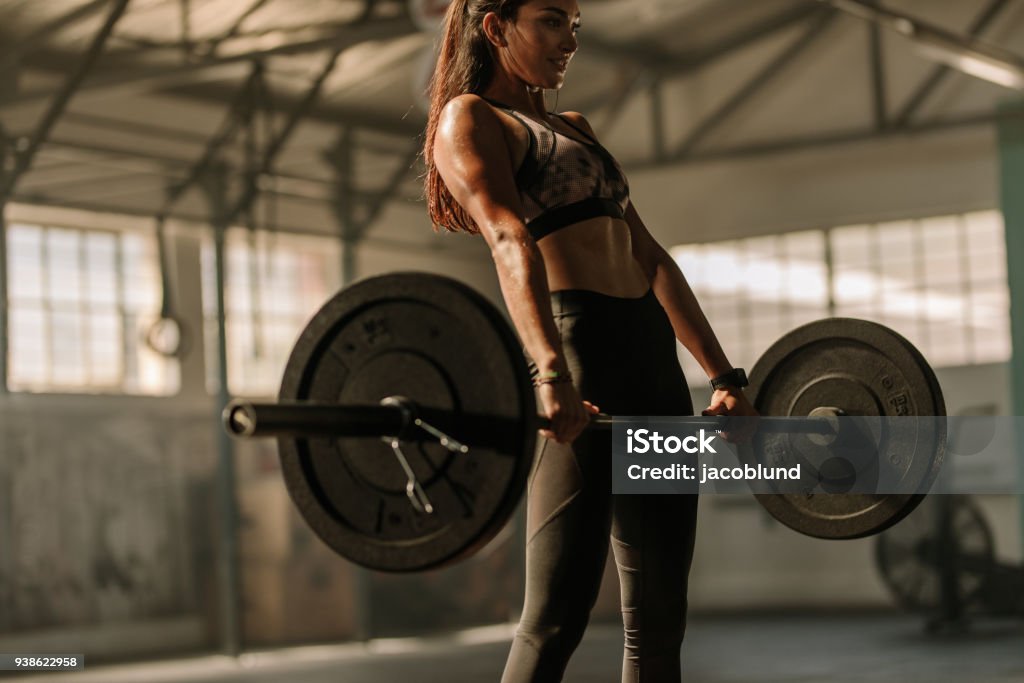 Determined and strong woman with heavy weights Determined and strong fitness woman training with heavy weights in fitness club. Female athlete holding heavy weight barbell in gym. Weightlifting Stock Photo