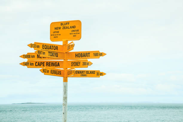 cima del poste indicador amarillo de nueva zelanda, con flechas apuntando a diferentes direcciones, los destinos más importantes, grandes ciudades como tokio, sydney, nueva york, hobart, kumagawa, stewart island, cape reinga, ecuador - global communications directional sign road sign travel fotografías e imágenes de stock