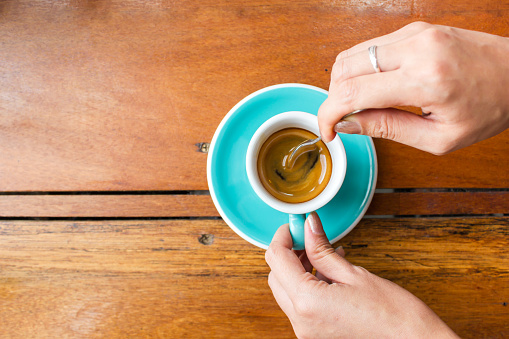 Woman using spoon stir espresso coffee in blue cup. Top view with copy space on wooden table. Food and drink background.