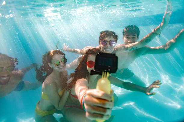 Group of young people taking selfie underwater Woman taking selfie of friends with waterproof camera under the water in swimming pool. Group of young people swimming underwater and making self portrait. waterproof photos stock pictures, royalty-free photos & images