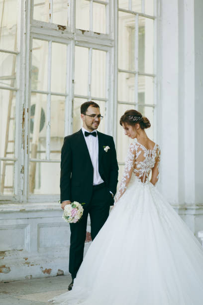 beau mariage photosession. marié en costume noir et jeune mariée en robe de dentelle blanche avec panache long avec une coiffure exquis en intérieur vintage sur la véranda d’une vieille maison avec des colonnes - veil bride lace married photos et images de collection