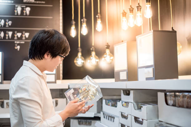 young asian man choosing package of electrical light bulb in warehouse - light shop imagens e fotografias de stock