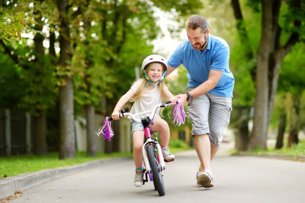 feliz padre enseñando a su pequeña hija a montar en bicicleta. niño aprendiendo a andar en bicicleta. - people caucasian sport family fotografías e imágenes de stock