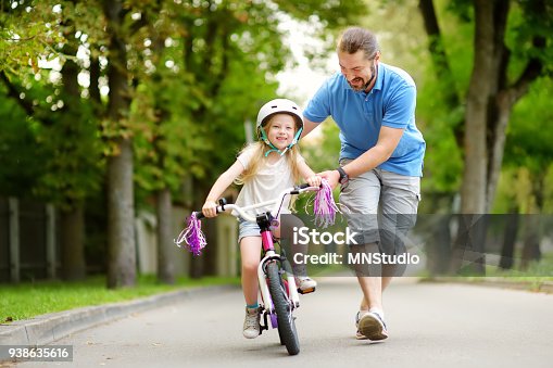 istock Happy father teaching his little daughter to ride a bicycle. Child learning to ride a bike. 938635616