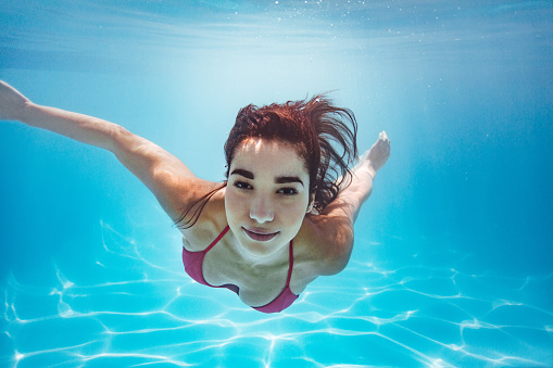 Beautiful woman swimming underwater in pool. Female swimmer in bikini at holiday resort.
