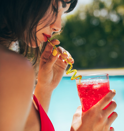 Close up of woman drinking cocktail at the poolside. Female having a drink while by the swimming pool.