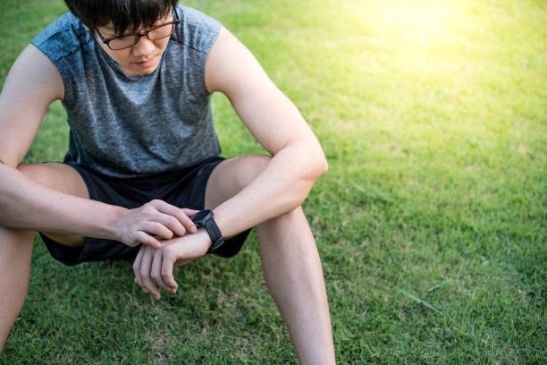 istock Young Asian man runner sitting on green grass looking at smart watch 938636416