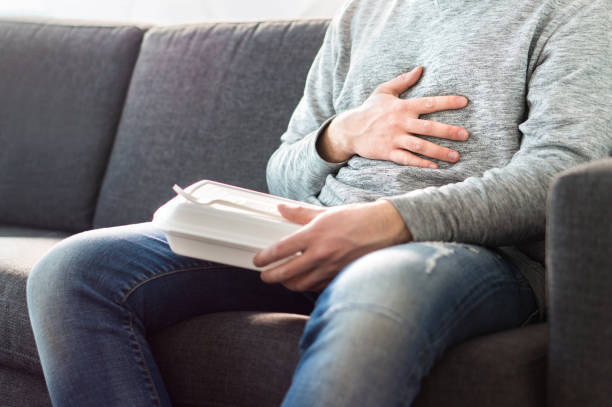 douleurs à l’estomac, intoxication alimentaire ou un problème de digestion après malbouffe rapide. l’homme a mangé trop et tient le ventre avec la main. - intoxication photos et images de collection