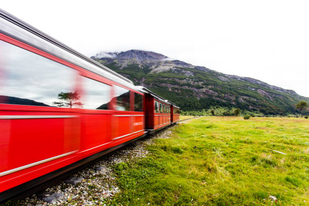 istock Long exposure of red train riding along green grassy field 938649320