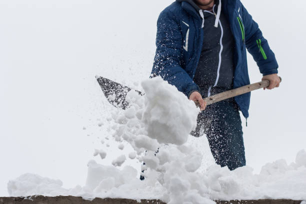 Young man clean a roof from snow by shovel. Spring snow removing after blizzard. stock photo