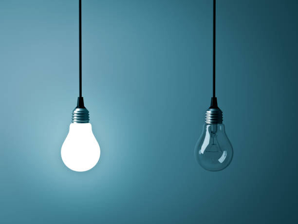 istock Two hanging light bulbs , One glowing and one turned off on dark green blue background 938669728