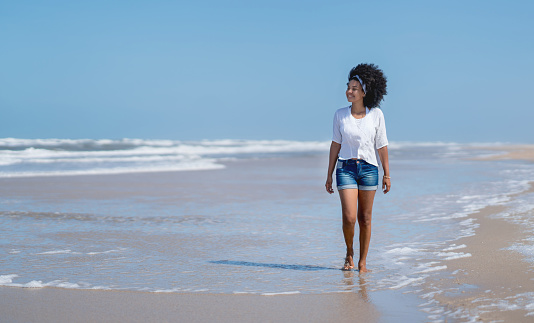 Beautiful African American young woman walking at the beach and looking very happy - lifestyle concepts