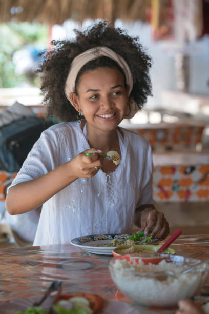 mulher brasileira, comendo em um restaurante na praia e olhar feliz - real people young women women beautiful - fotografias e filmes do acervo