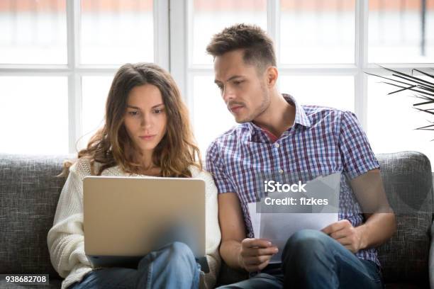 Focused Worried Couple Paying Bills Online On Laptop With Documents Stock Photo - Download Image Now