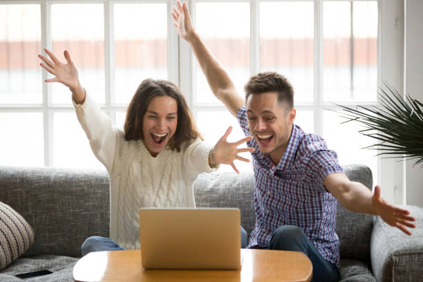 istock Young couple feeling excited by online win looking at laptop 938682758