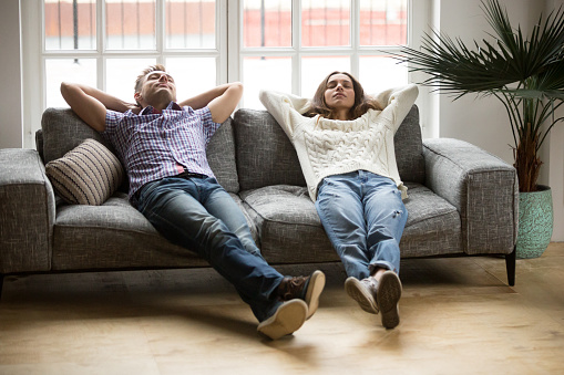 Young couple relaxing having nap or breathing fresh air, relaxed man and woman enjoying rest on comfortable sofa in living room, happy family leaning on soft couch taking break for dozing together