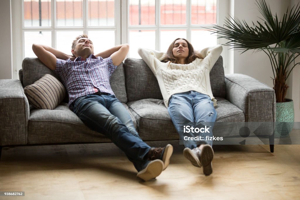 Young couple relaxing together on sofa enjoying nap breathing air Young couple relaxing having nap or breathing fresh air, relaxed man and woman enjoying rest on comfortable sofa in living room, happy family leaning on soft couch taking break for dozing together Sofa Stock Photo