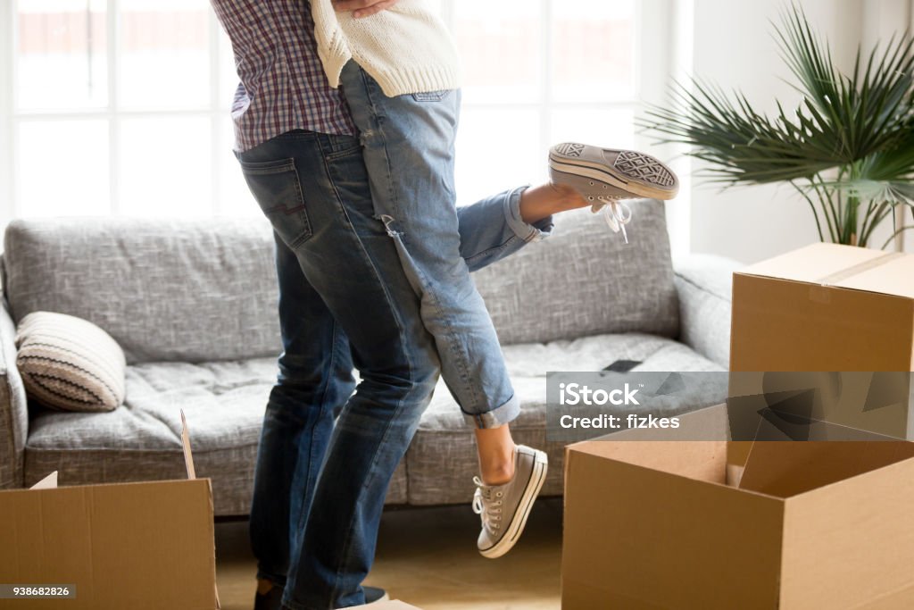 Man lifting woman standing among cardboard boxes, close up view Happy couple on moving day concept, man lifting woman standing among cardboard boxes starting living together in new own house, husband holding embracing wife celebrating relocation, close up view Moving House Stock Photo
