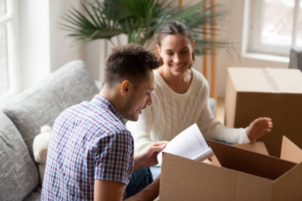 istock Young man holding book helping wife packing on moving day 938682866