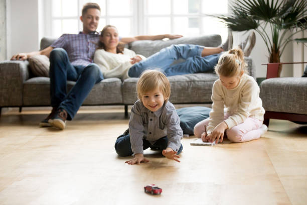bambini che giocano a terra, genitori che si rilassano sul divano a casa - floor two parent family couple home interior foto e immagini stock