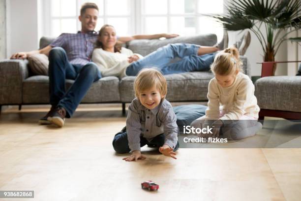 Kids Playing On Floor Parents Relaxing On Sofa At Home Stock Photo - Download Image Now