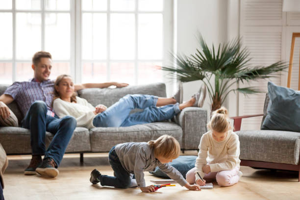 dzieci rodzeństwo gra rysunek razem, podczas gdy rodzice relaks w domu - childrens furniture zdjęcia i obrazy z banku zdjęć