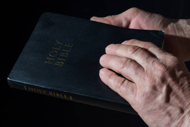 istock Aged man's hands holding the Bible. Low key light 938683652