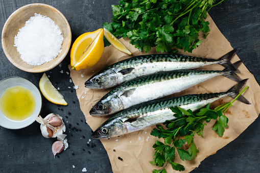 Fresh mackerel fish on paper with lemon, salt, olive oil, garlic, parsley and pepper. Top view