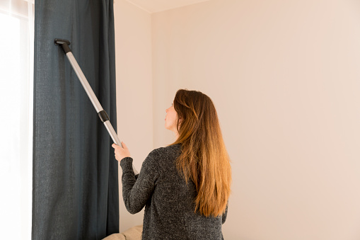 People, housework and housekeeping concept - woman with vacuum cleaner at home. Curtain cleaning. Spring cleaning