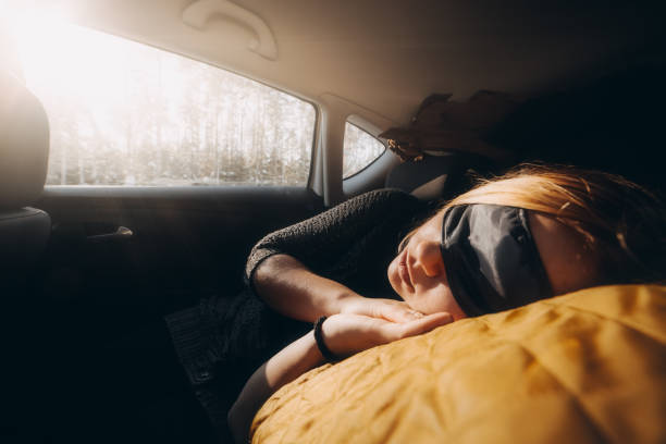 Woman is sleeping inside of car at sunset. Using sleeping mask blindfold. Automotive travel stock photo