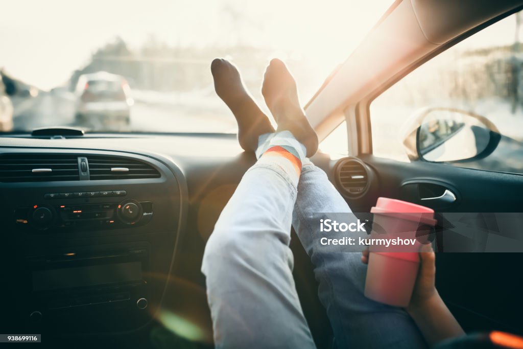 Femme tient la tasse de café à l’intérieur de la voiture. Parcourez le mode de vie. Jambes sur le tableau de bord - Photo de Voiture libre de droits