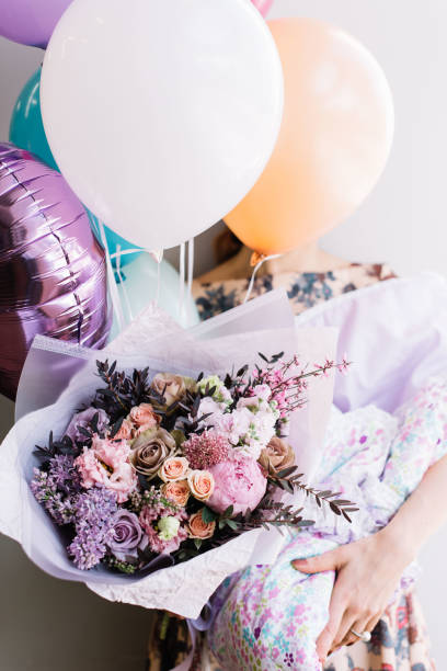 woman holding a colourful flower bouquet, balloons and a baby cover for a newborn stock photo