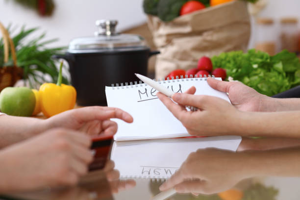 istock Closeup of human hands cooking in kitchen. Women discuss a menu using block note. Copy space area. Healthy meal, vegetarian food and lifestyle concepts 938713566