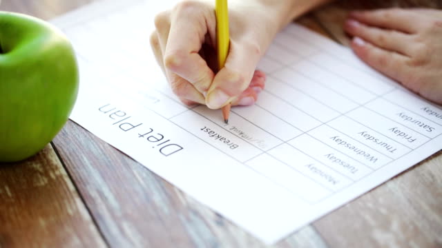 close up of young woman writing diet plan at home