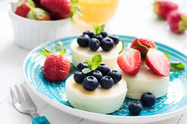 Mini cheesecake with fresh strawberries and blueberries on blue plate, closeup view. Syrniki, cottage cheese pancakes