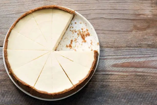 Photo of New York Cheesecake or Classic Cheesecake sliced on rustic wood, top view