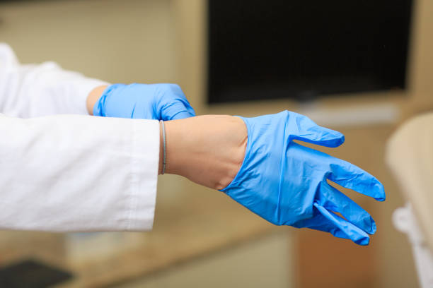 médico vestido de guantes en las manos en el fondo de la sala de operación. enfermera real poner guantes estériles. trabaja en clínica con guantes estériles. protocolo médico para los empleados de enfermería. - guante quirúrgico fotografías e imágenes de stock