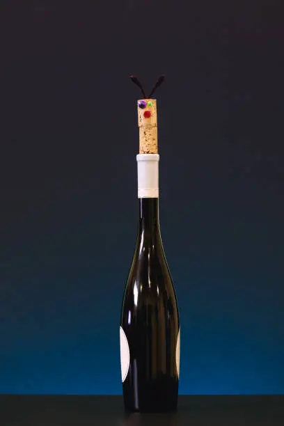 Funny cork stopper on top of wine bottle. Picture of cork stopper and wine bottle on fancy background. Alcohol intoxication concept for banners, posters and other design projects.