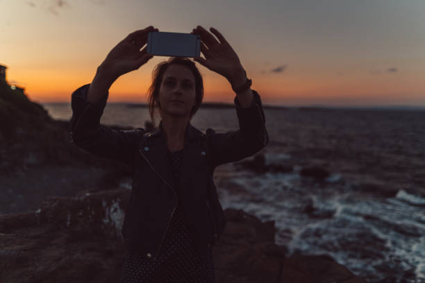 Woman on beach holiday taking photos with smartphone on sunset