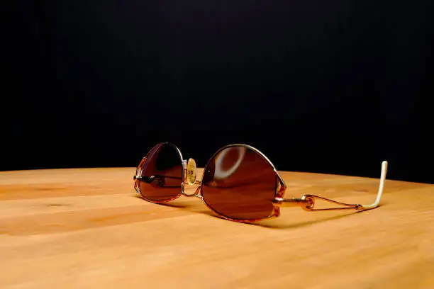 A pair of tinted glasses resting on a wooden desk with a black background